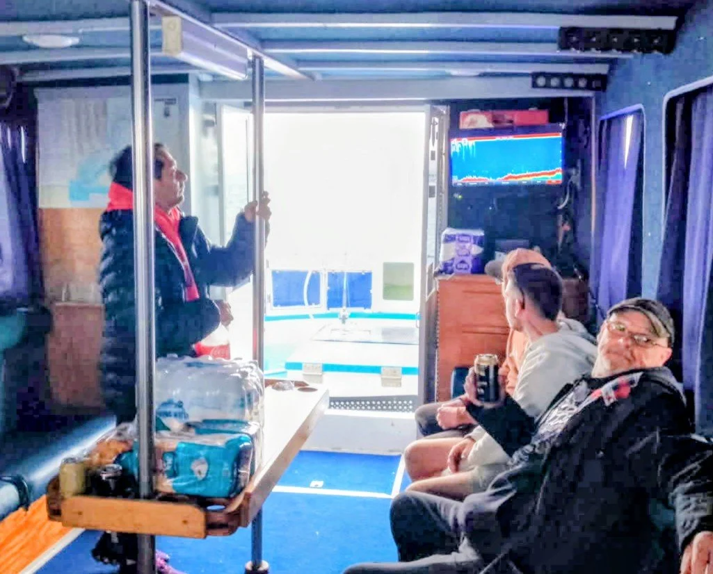 Inside a boat cabin with three men sitting on the right, one holding a drink. Day Trip Fishing experience on Westernport Bay, with Out there fishing charters