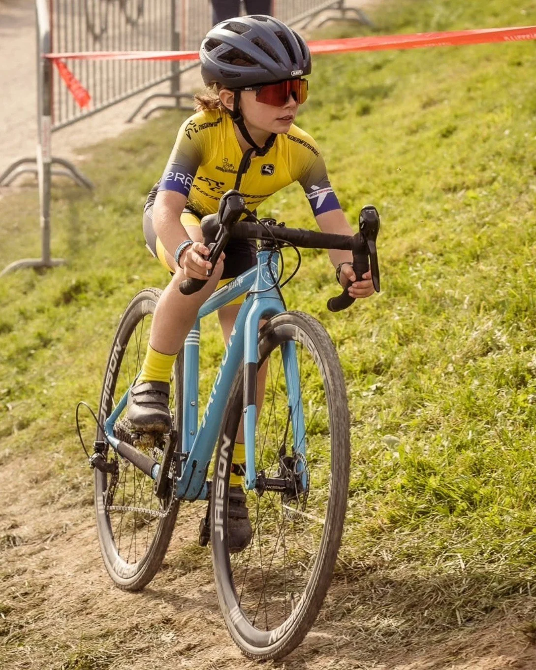 Junge Radfahrerin in Fahrradtrikot, Helm und Sonnenbrille auf einem Mountainbike im Gelände bei einem Rennen.