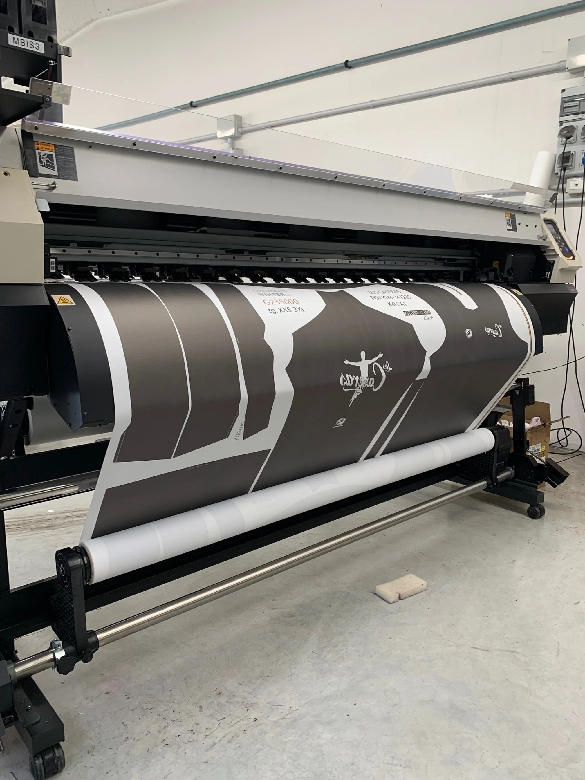 Großdruckplotter druckt ein farbiges Bild mit schwarz, Weiß und anderen Farben auf Papier. Der Drucker befindet sich in einer Werkstatt oder Druckerei.