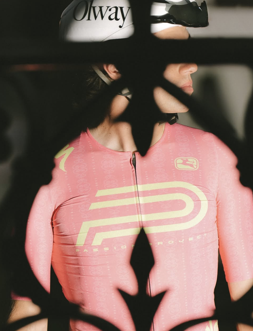 Eine Frau in einem rosa Radtrikot mit einem Helm, gesehen durch ein Gitternetz.