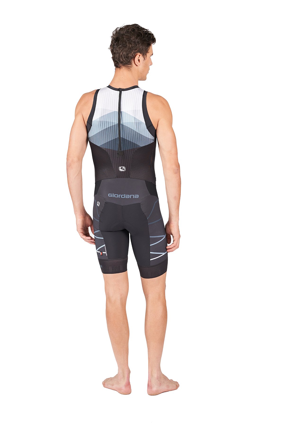 Ein männlicher Athlet in einem schwarzen Triathlon-Einteiler, steht barfuß, mit Blick nach rechts, vor weißem Hintergrund.