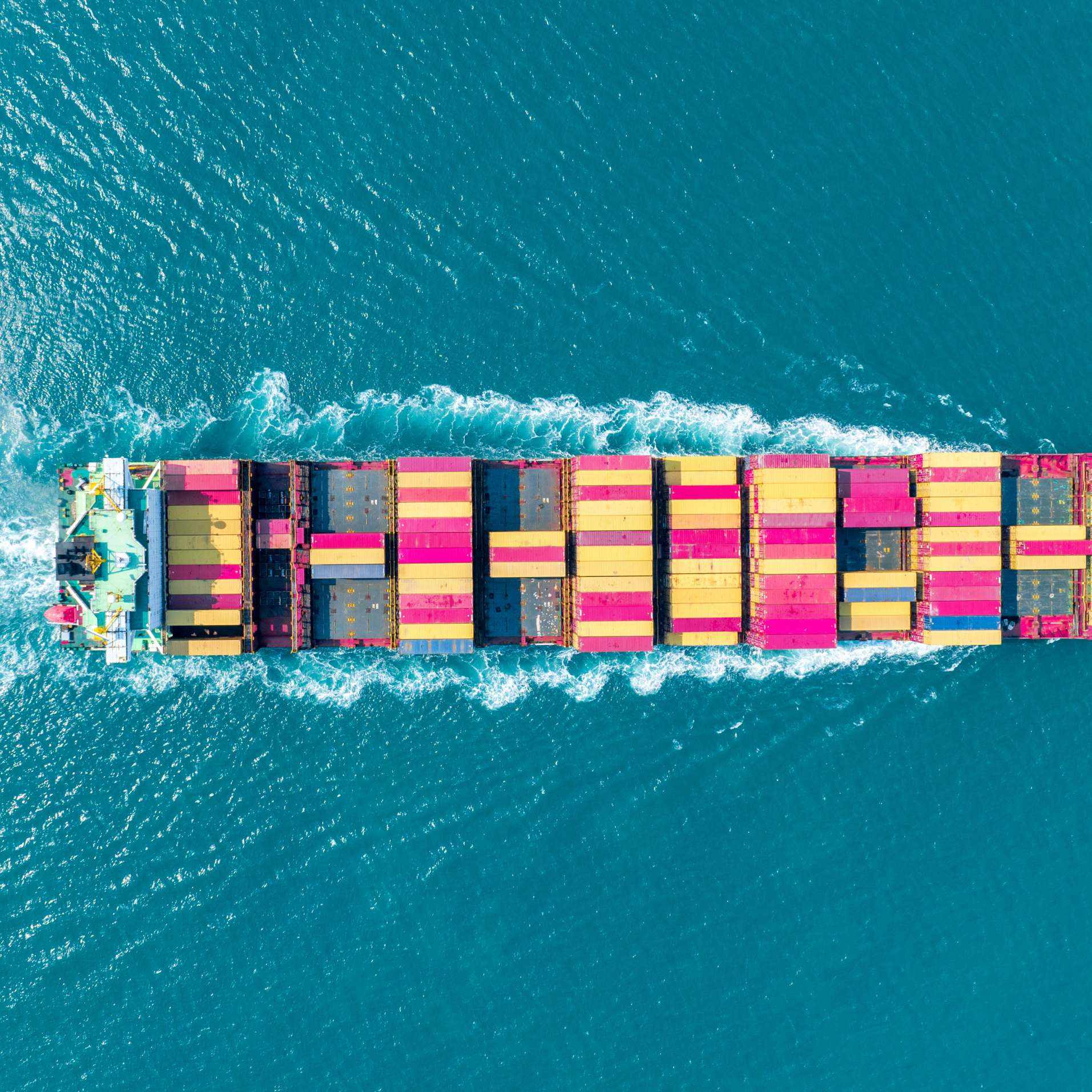Aerial view of a cargo ship with multicolored containers sailing in turquoise water.