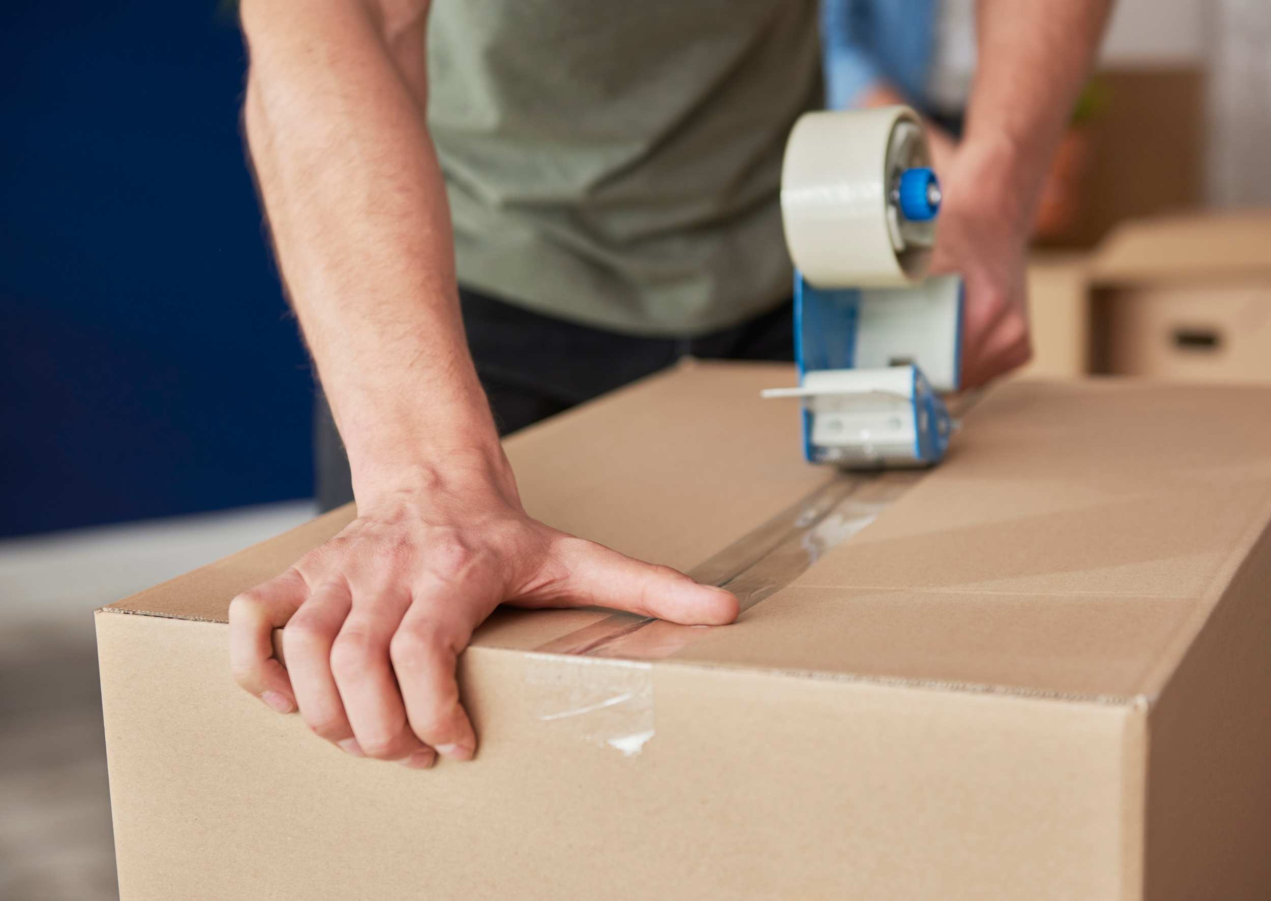 A person sealing a cardboard box with packing tape using a tape dispenser.