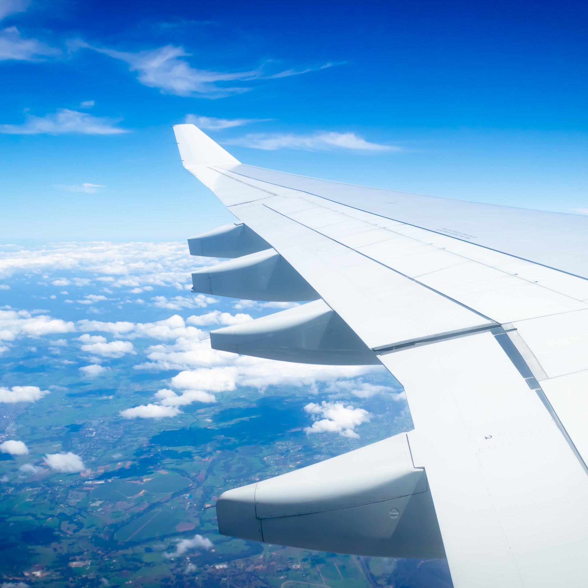 View of an airplane wing flying above clouds and green landscape.