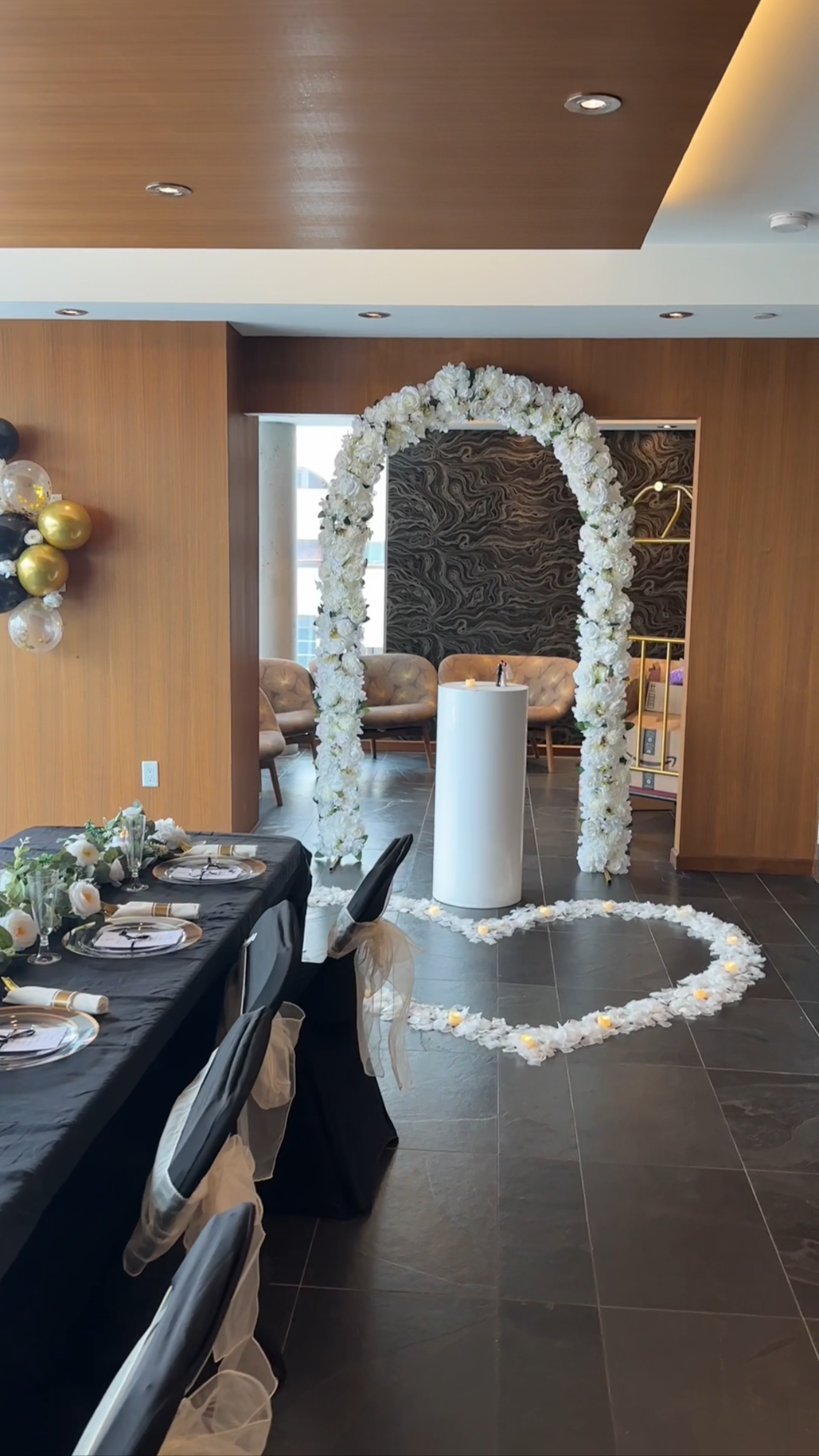 A decorated event space with a floral arch, a candle, and a heart-shaped flower arrangement on the floor, indicating a wedding or romantic celebration.