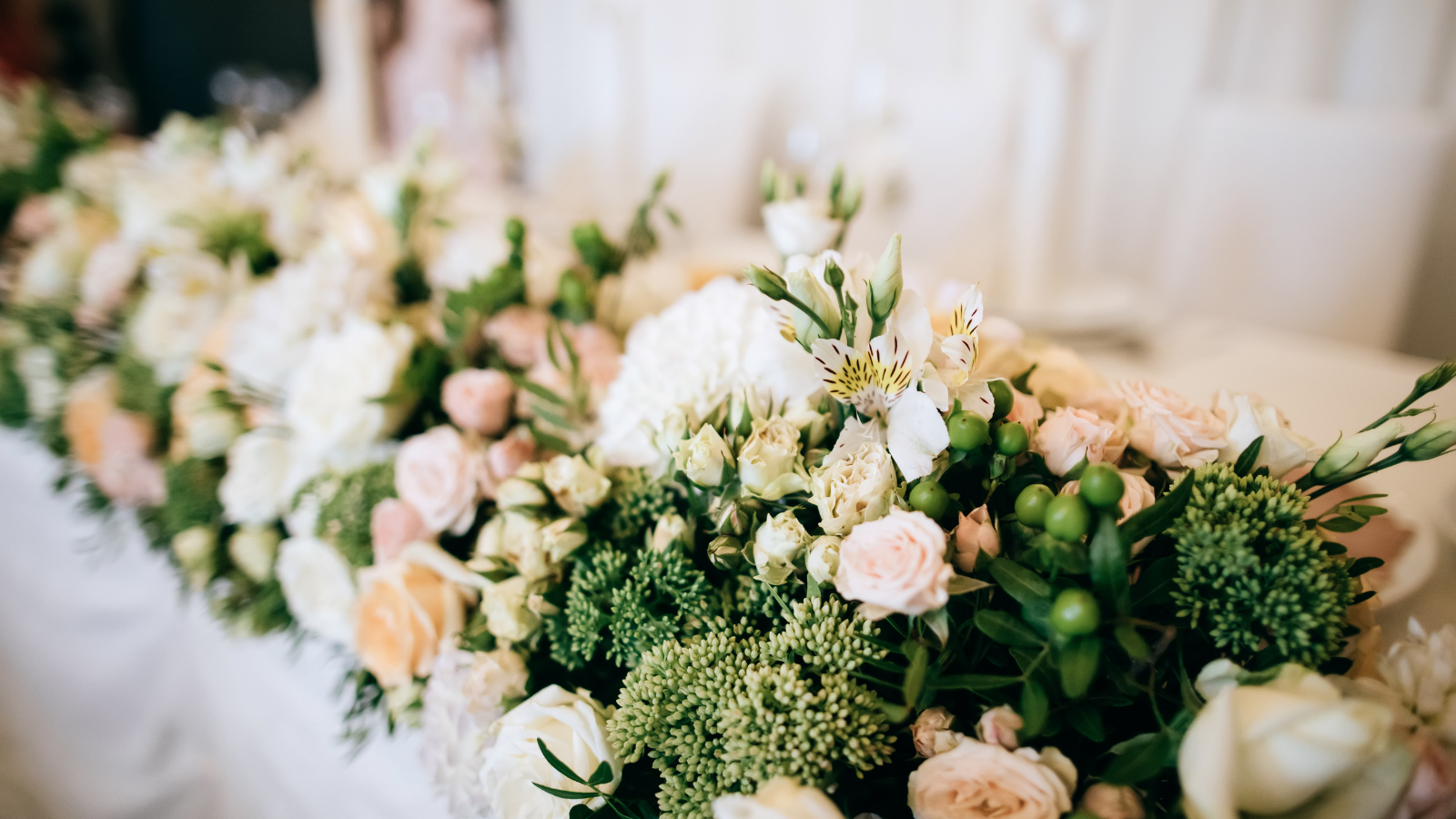 A close-up view of a floral arrangement with white, pink, and green flowers, featuring roses, lilies, and greenery, likely for a wedding or special event.