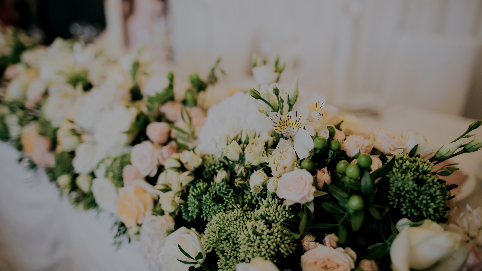 A close-up of a floral arrangement with white, peach, and green flowers, including roses, hydrangeas, and greenery, on a table.