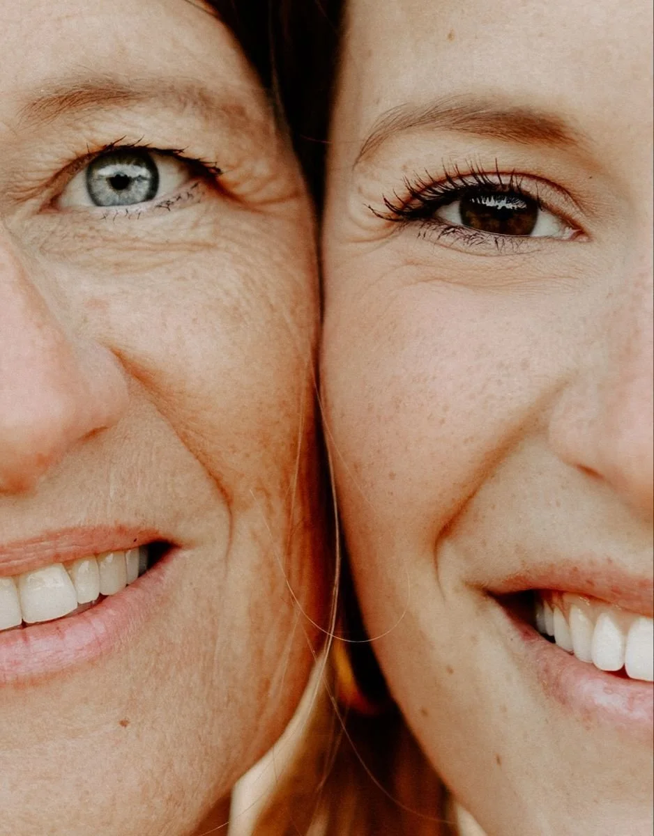 Close-up of two women smiling, with their faces touching, showing their eyes, noses, and smiles.