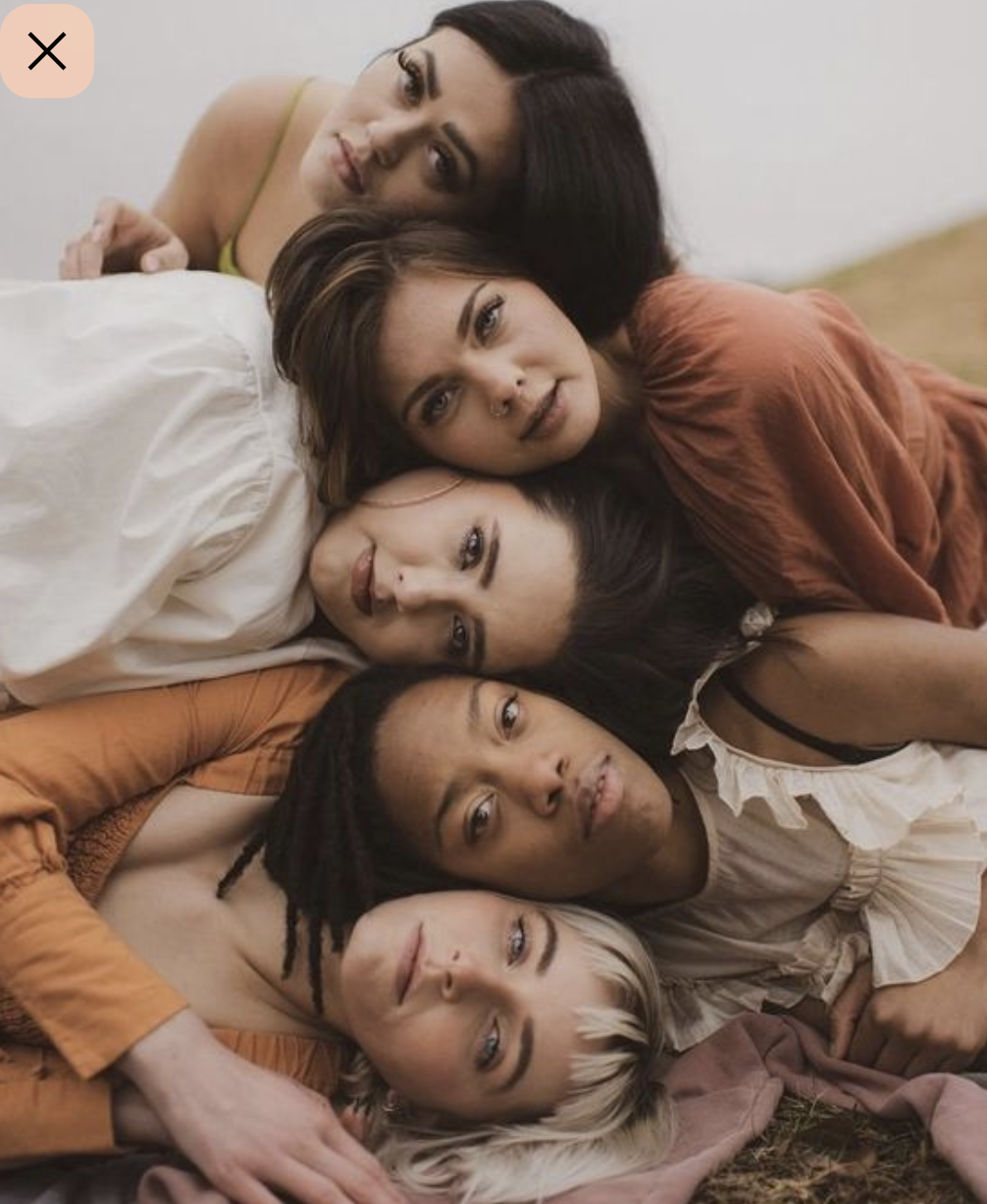 Five women lying on the ground with their heads stacked close together, looking at the camera.