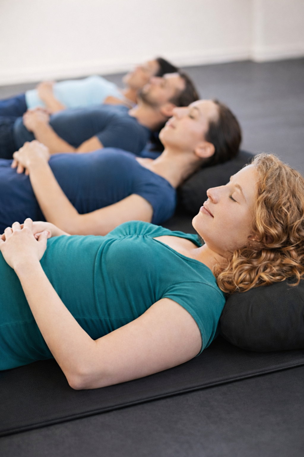 Four people lying on their backs with eyes closed on yoga mats, practicing meditation.