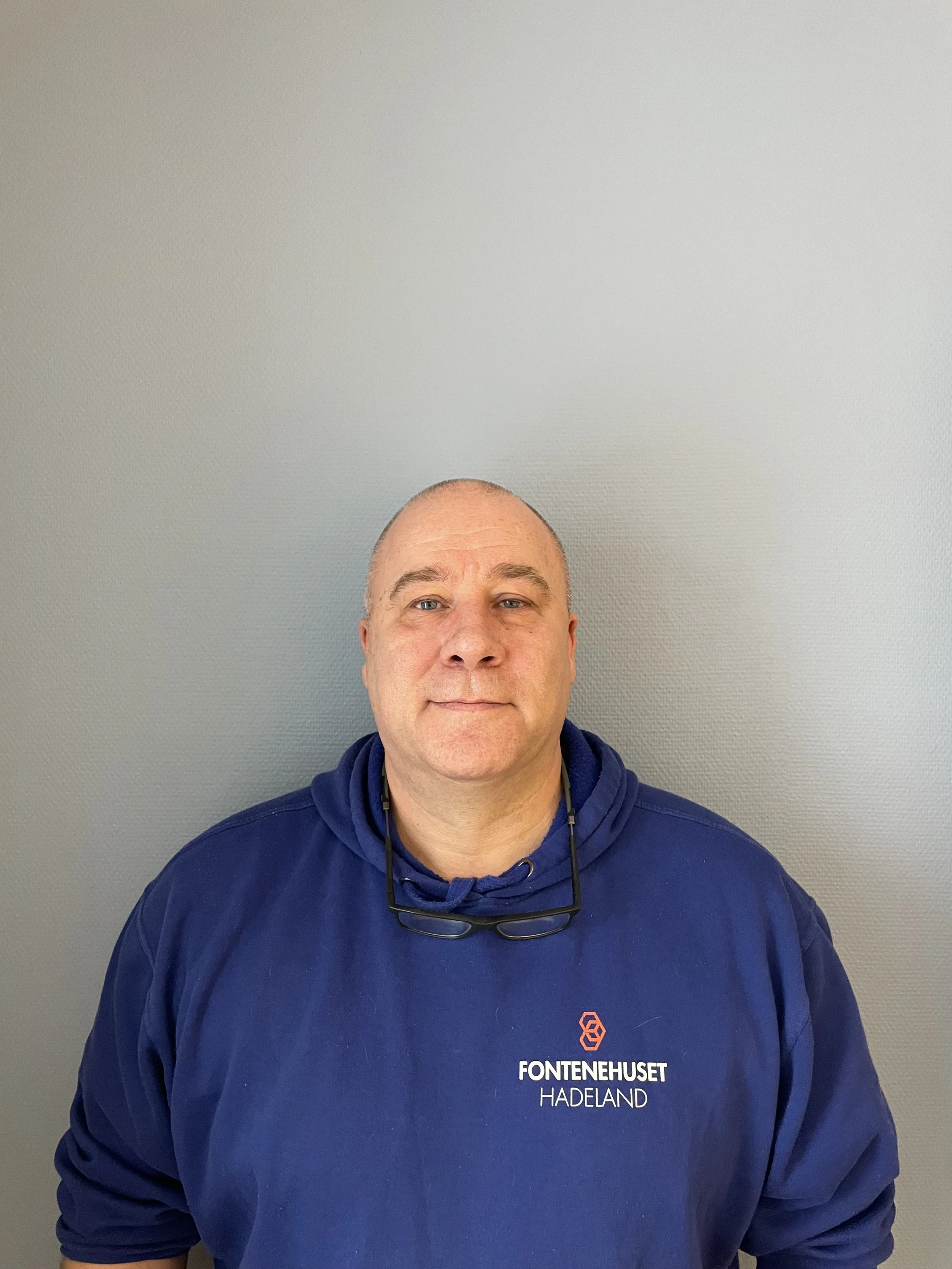 En mann med blå hettegenser med tekst 'FONTEHUSE Hadeland' står foran en grå vegg.
