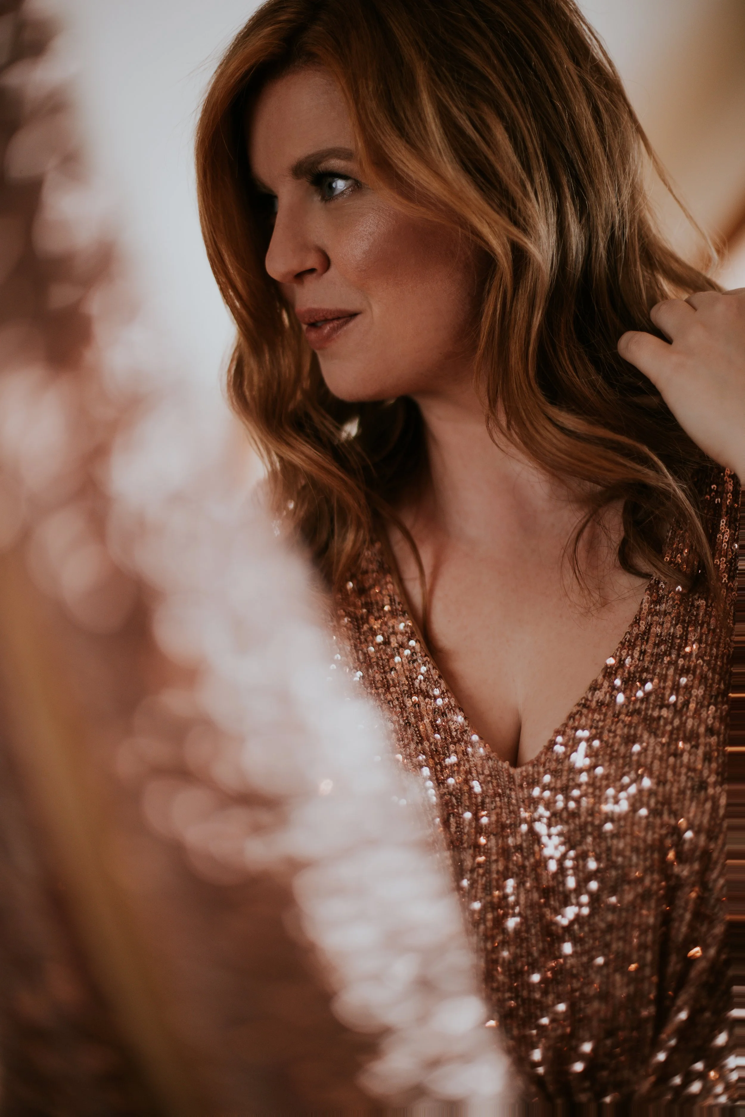 Eine Frau mit roten, lockigen Haaren trägt ein glitzerndes, kupferfarbenes Kleid.