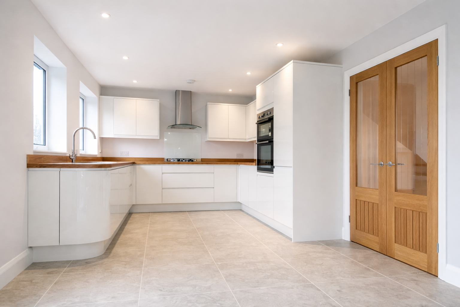 Modern kitchen with white cabinets, wooden countertops, a stainless steel range hood, built-in oven, and double wooden doors.