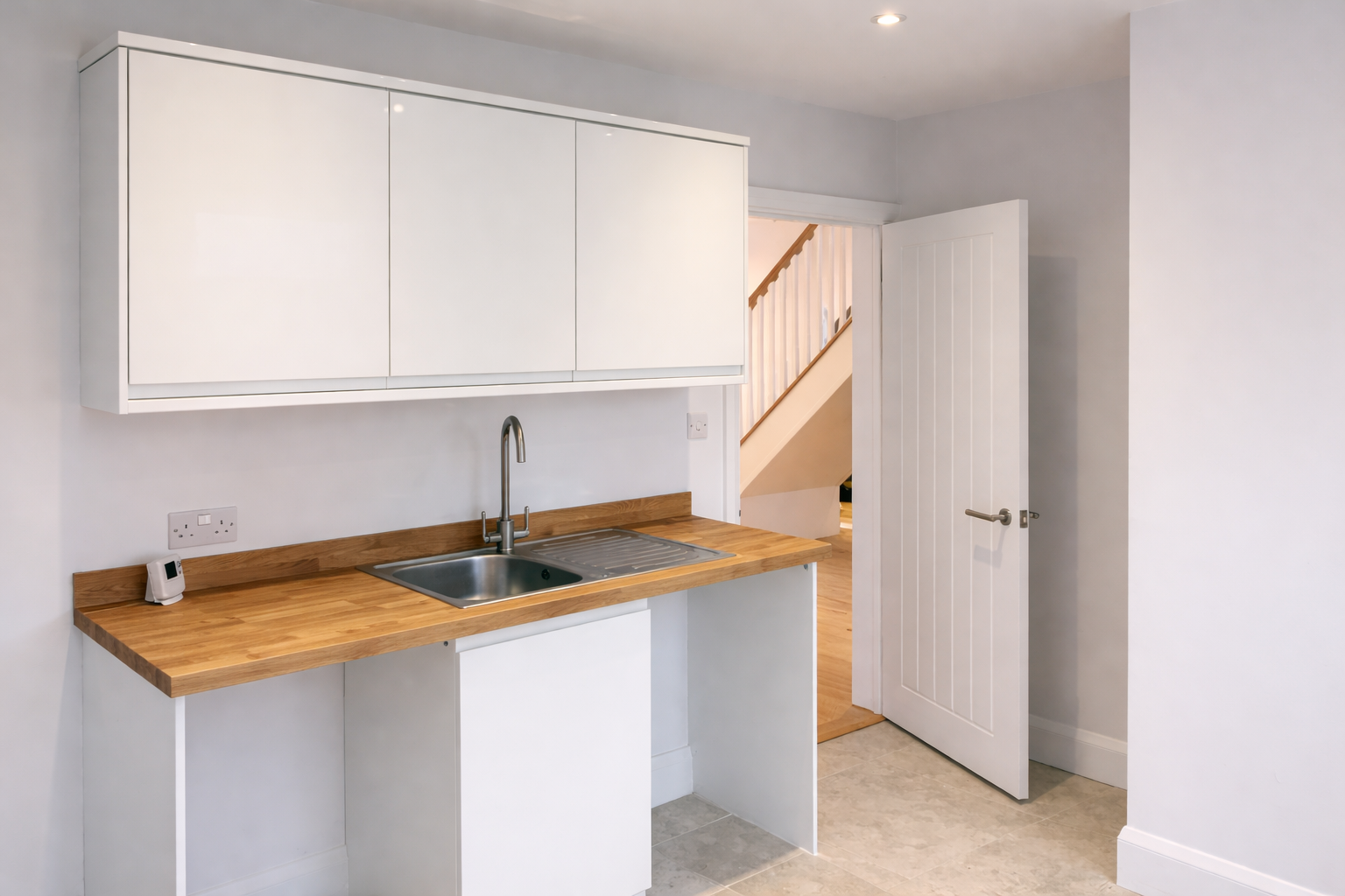 Kitchen with white cabinets, wooden countertop, stainless steel sink, and a door leading to a hallway with a staircase.