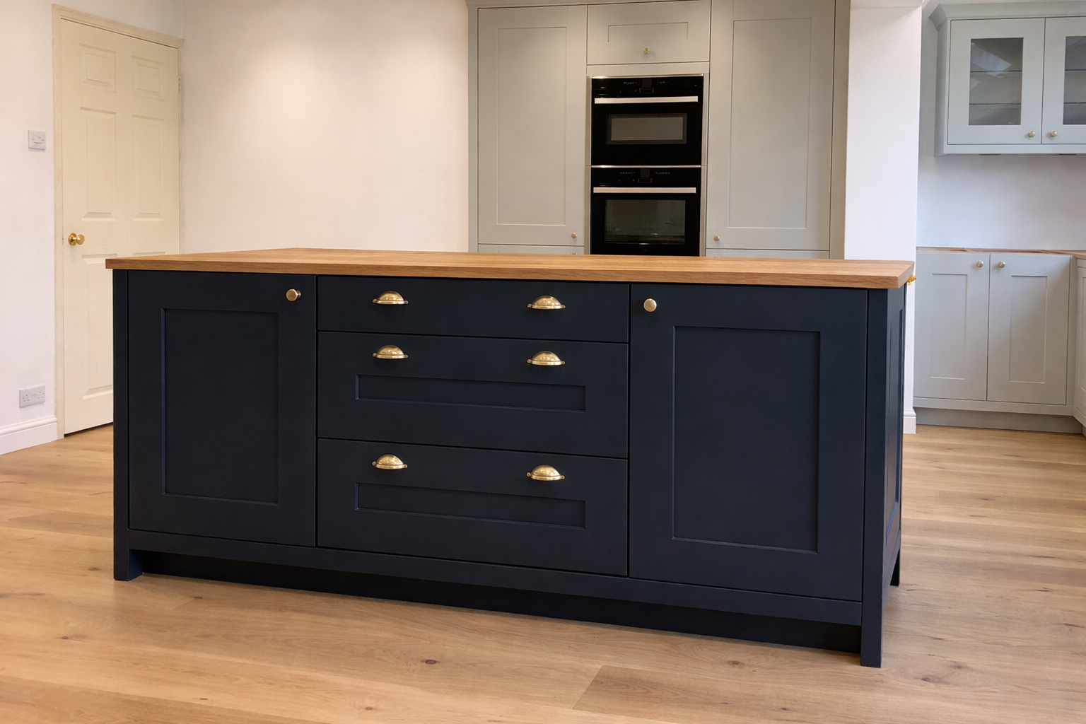 A modern kitchen island with navy blue cabinetry, a wooden countertop, and brass handles, set in a kitchen with white cabinets and hardwood flooring.