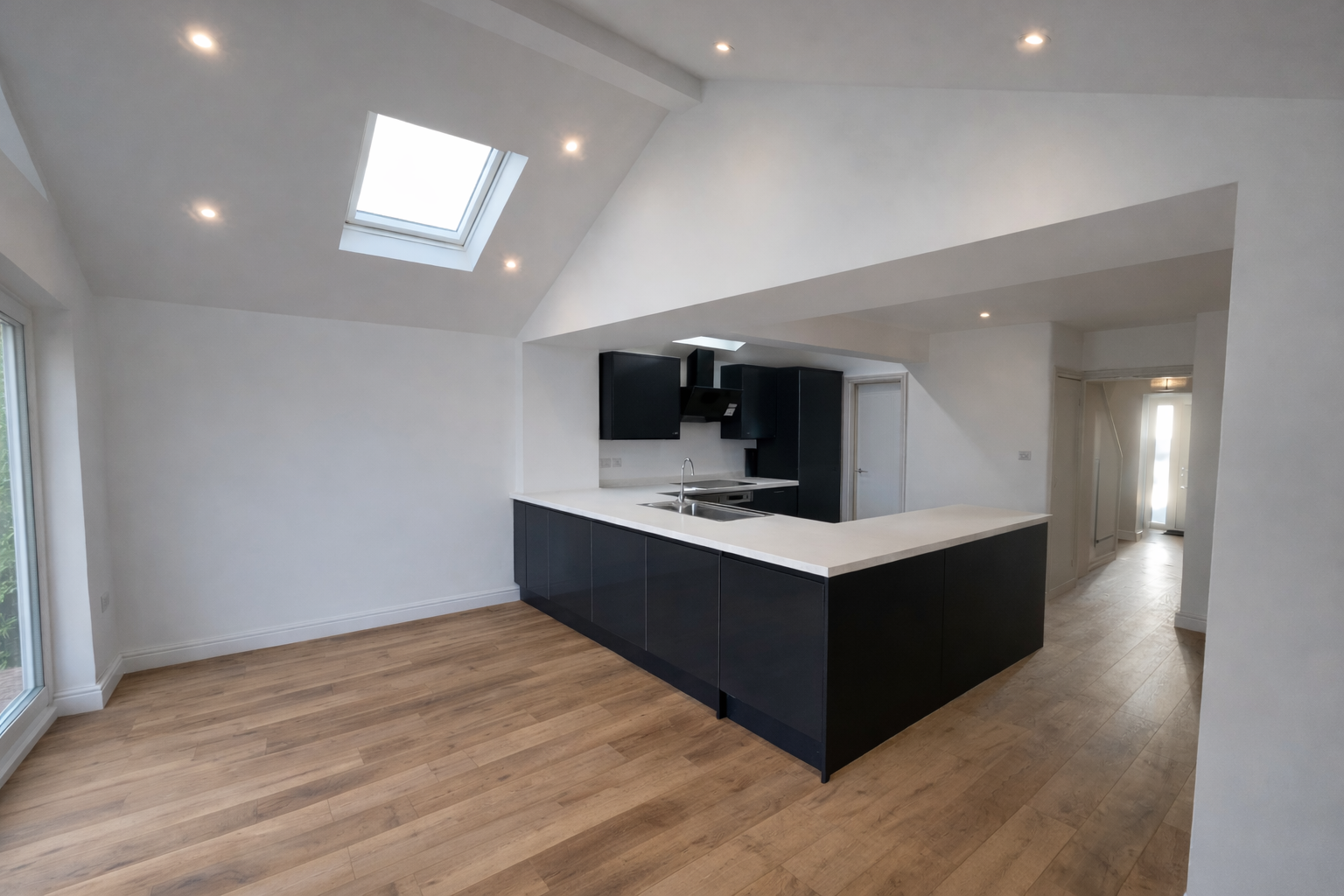 Empty modern kitchen with black cabinets, white countertops, and skylight, open space with natural wood flooring.