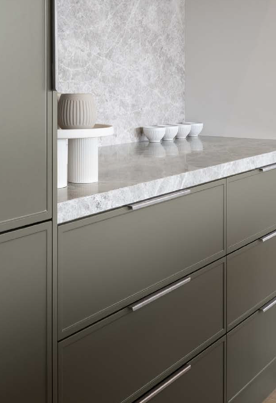 Close-up of a modern kitchen cabinet with a marble countertop and decorative vases and bowls.