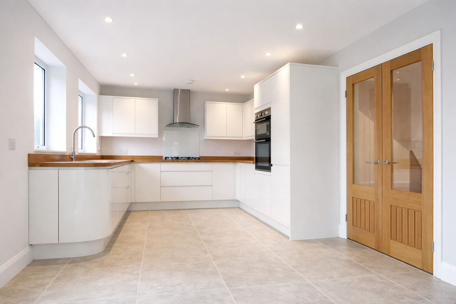 Modern kitchen with white cabinets, wooden countertops, built-in oven, gas stove, stainless steel range hood, and double glass-paneled wooden doors.
