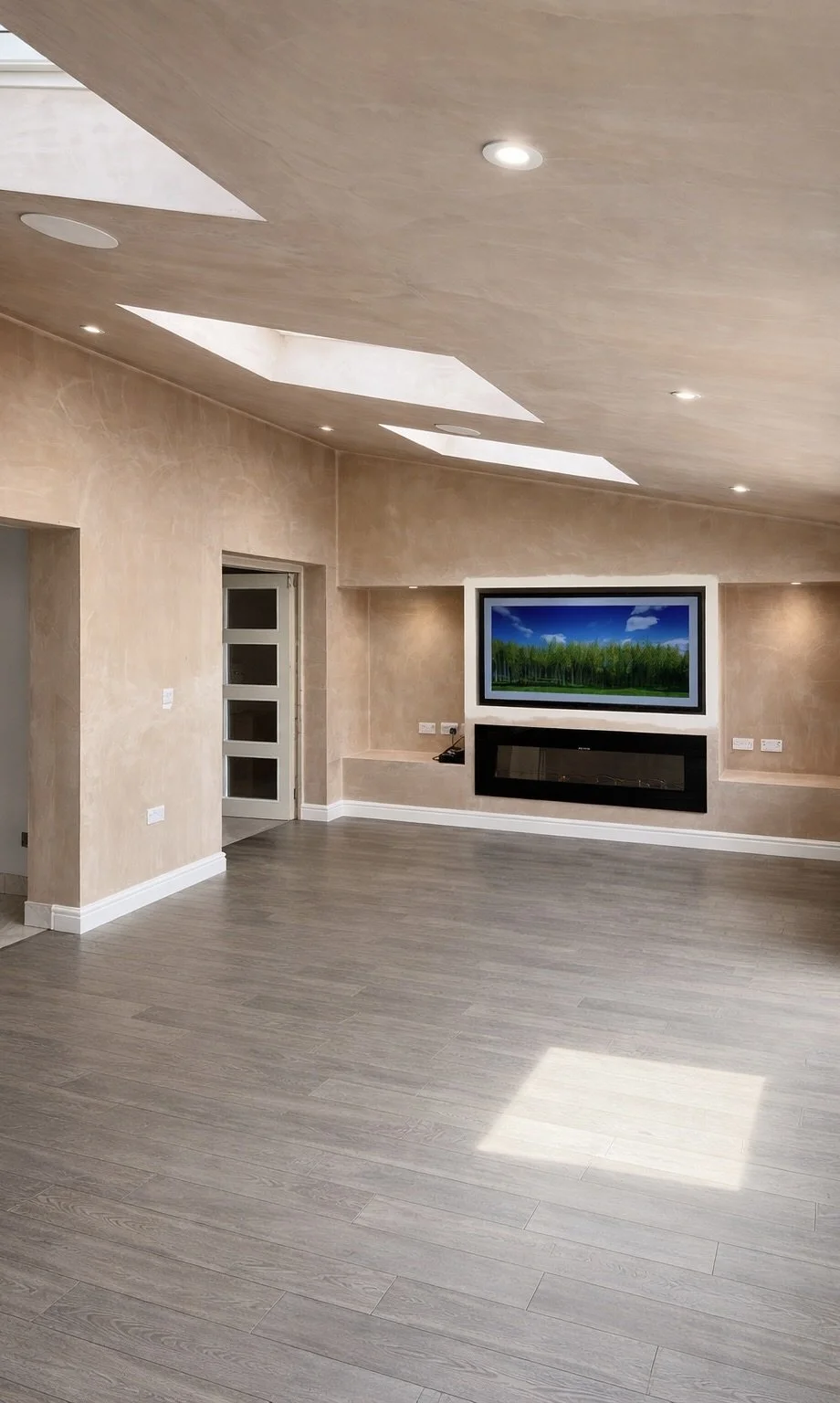 Empty living room with a mounted television, a modern electric fireplace below it, and natural light coming from skylights in the ceiling.