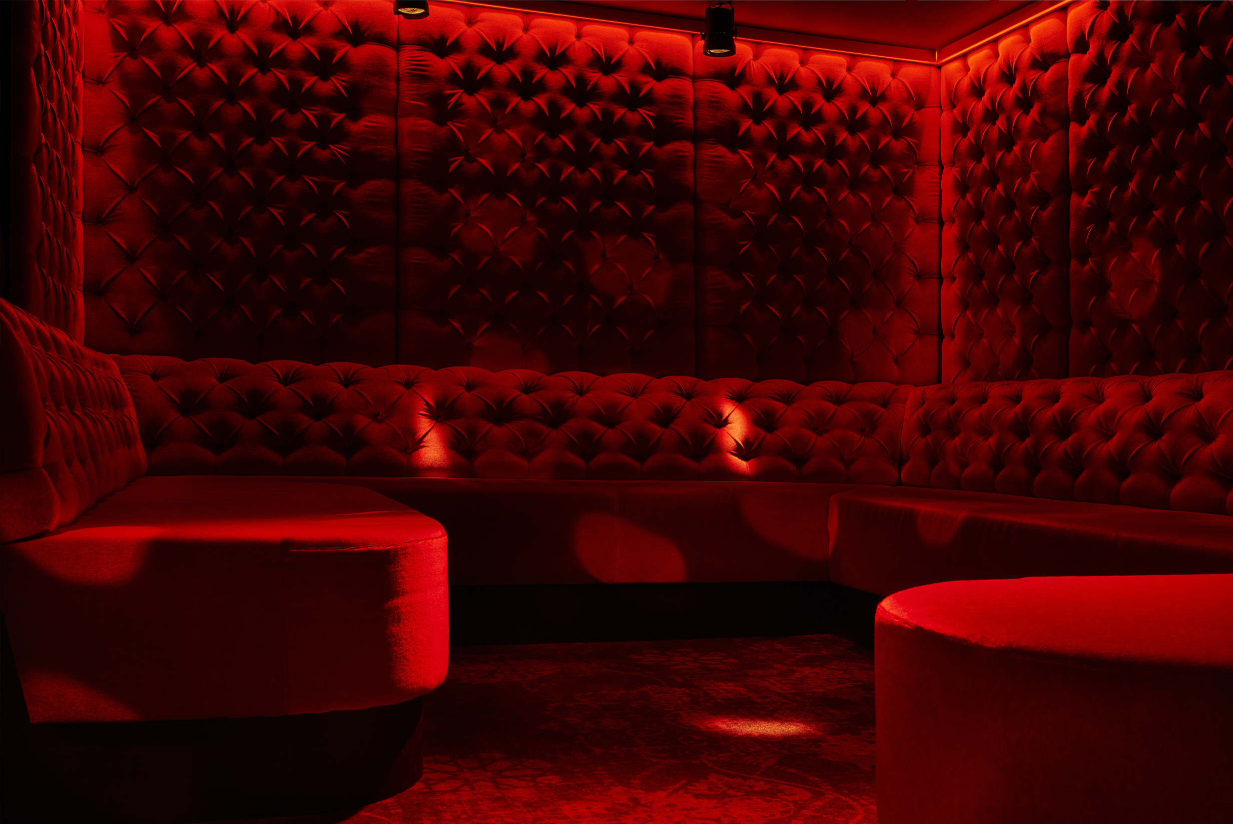 Red velvet tufted wall and seating area in a dimly lit lounge or club with warm lighting.