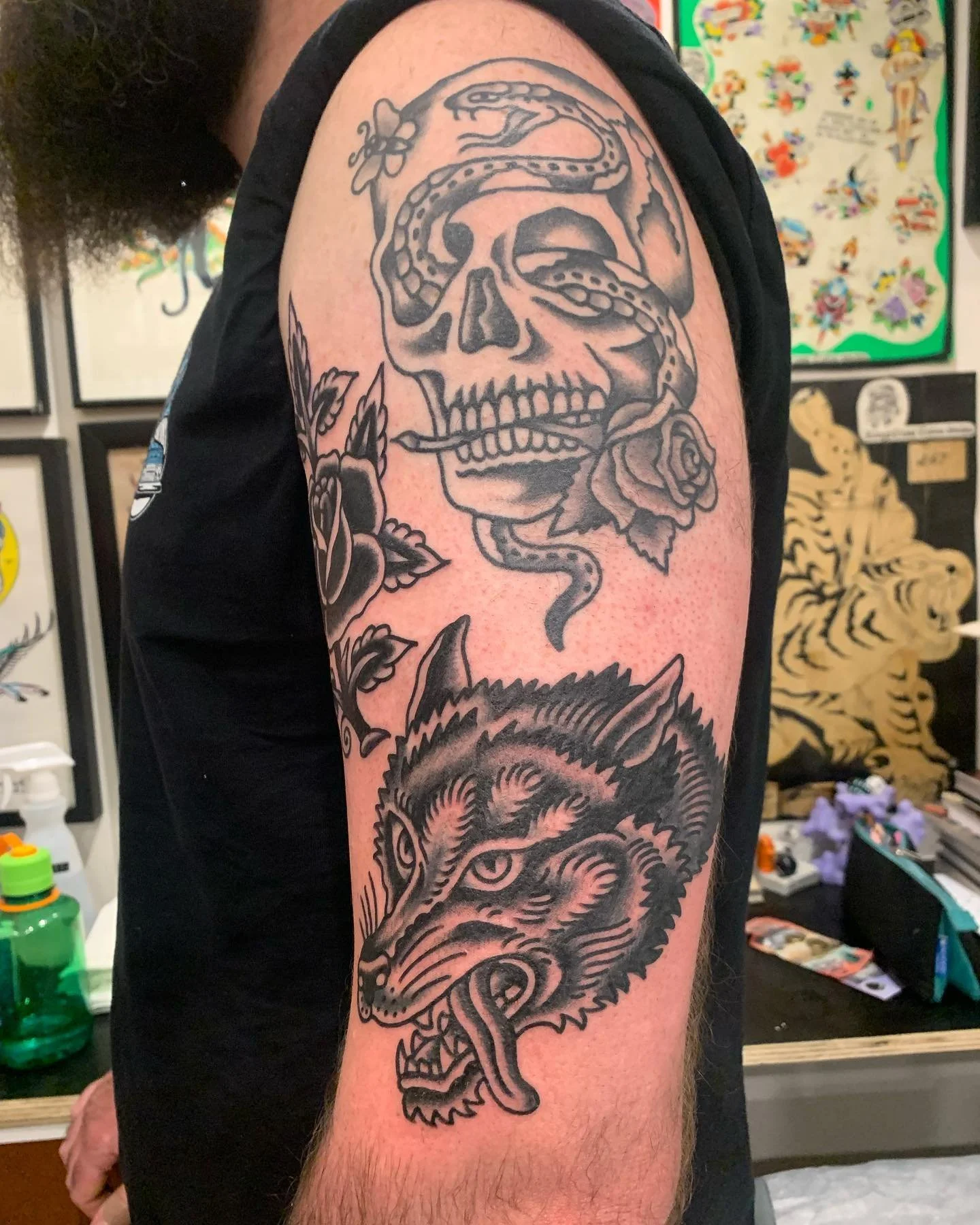 Tattoo of a skull with a snake coiled around it and a rose near the skull's mouth on a person's upper arm.