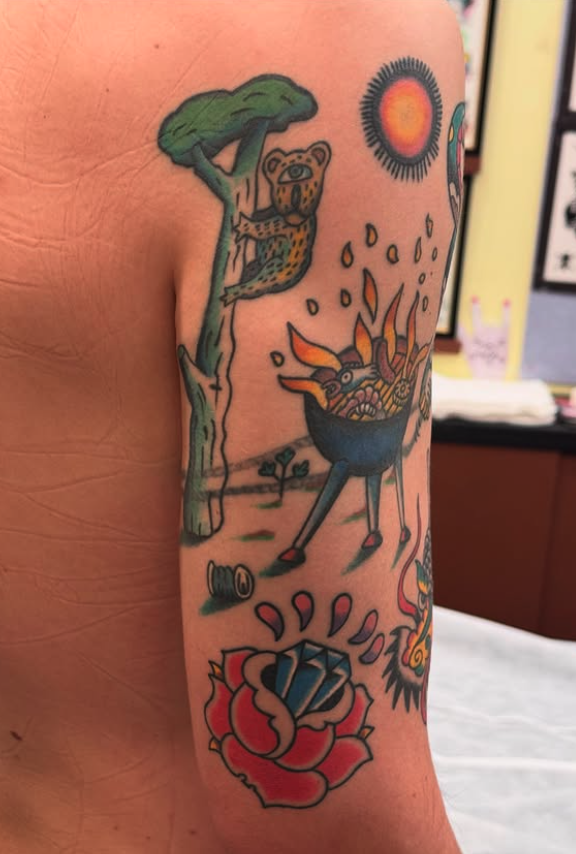 Colorful tattoo with a tree and a sitting cheetah, a sun, a bowl with flames and fire, and a blooming rose.