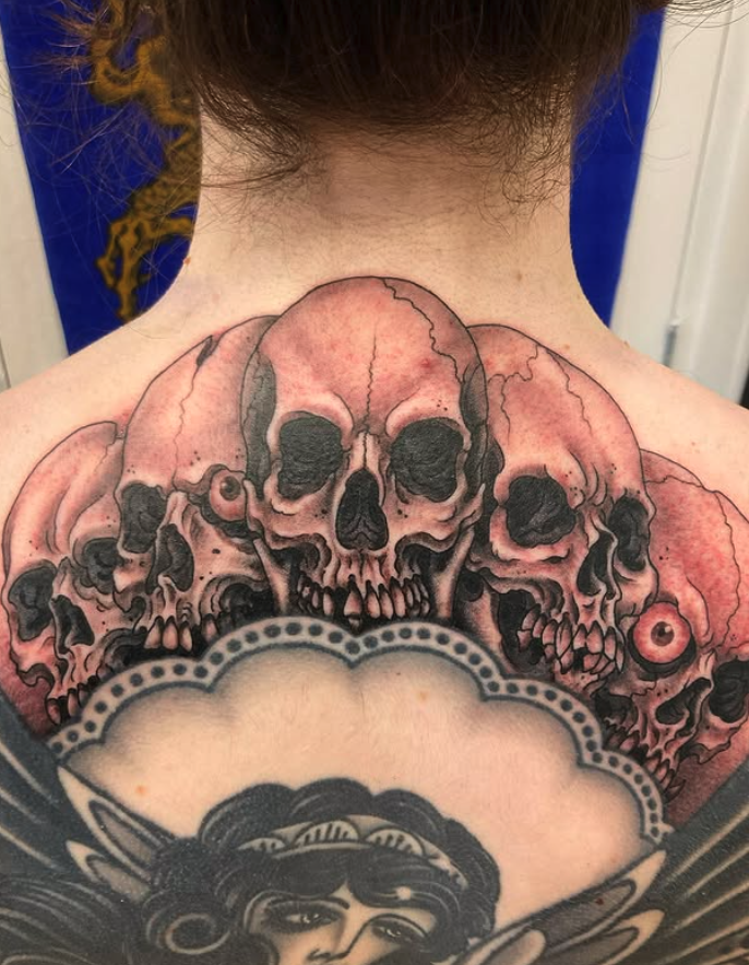 Tattoo of multiple skulls with black and red shading on a person's upper back and shoulders.