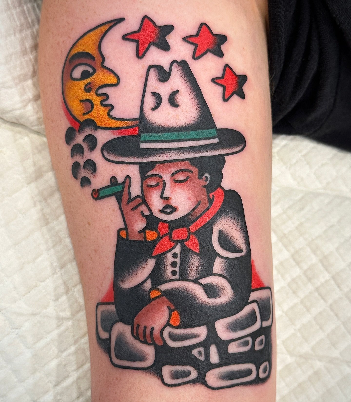 Tattoo of a woman with closed eyes, wearing a witch hat, holding a cigarette, with a moon, stars, and clouds in the background.