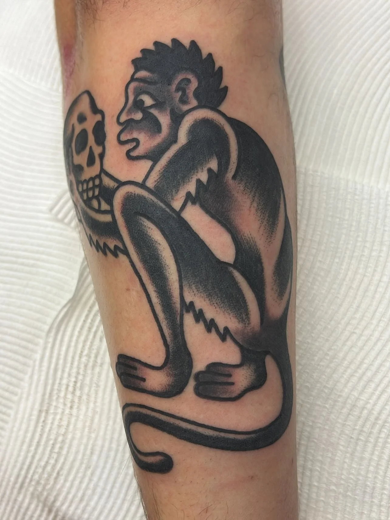 A tattoo of a person with a mohawk hairstyle, holding a skull, with bold black lines and shading.