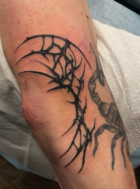 Tattoo of a cracked moon with a scorpion on a person's forearm.
