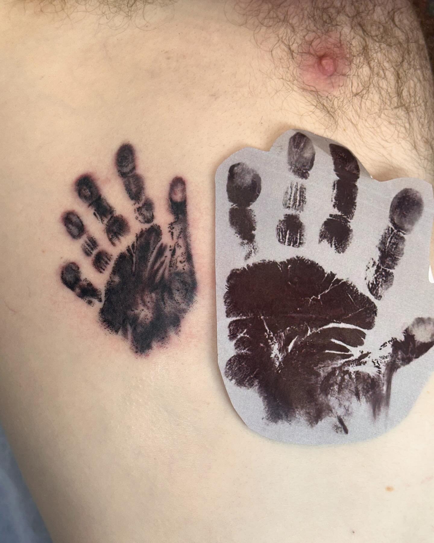 Tattoo of a handprint on a person's skin, with a stencil of a handprint held nearby.