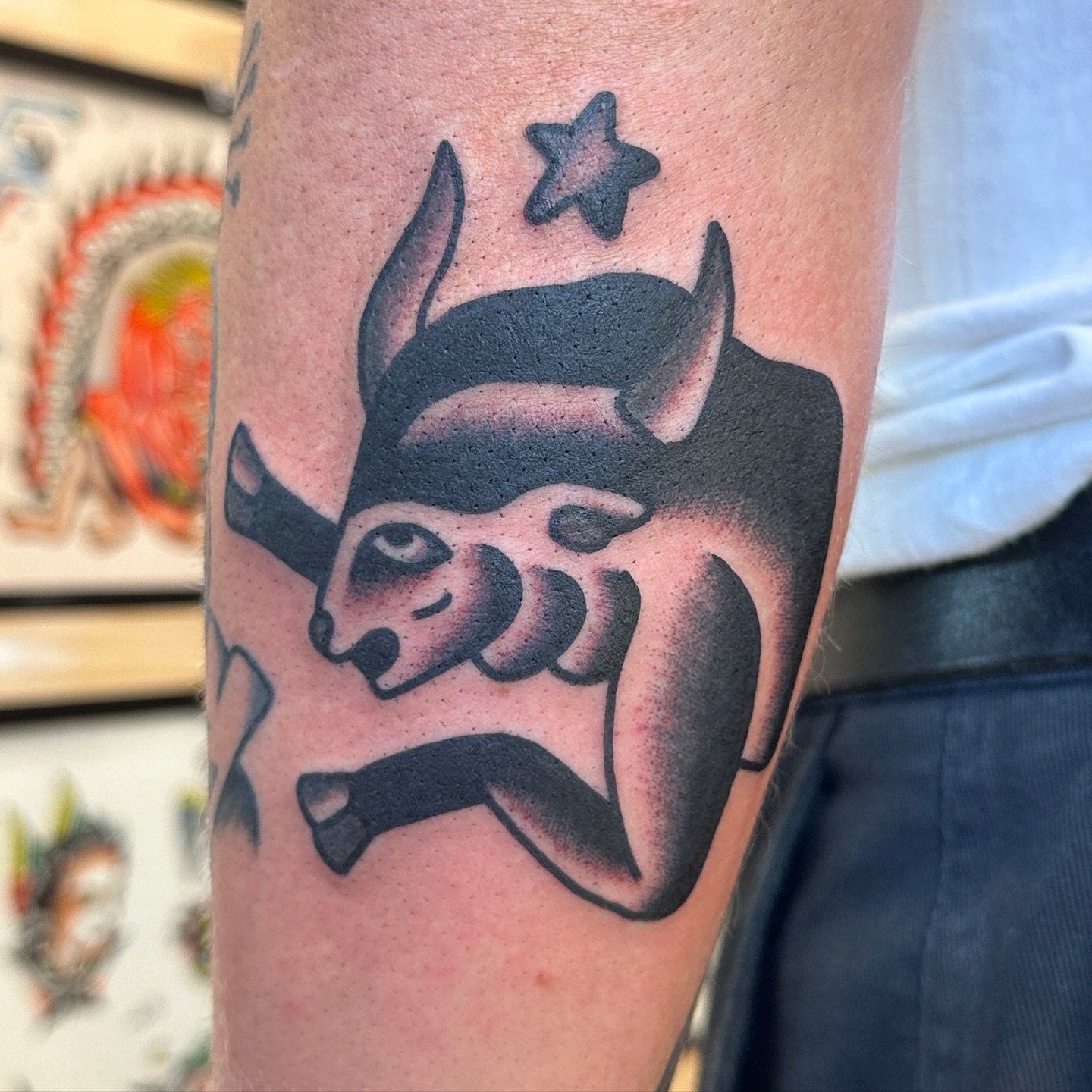 Tattoo of a cat with a unicorn horn, eyepatch, and tail, holding a sword, with a star above its head.