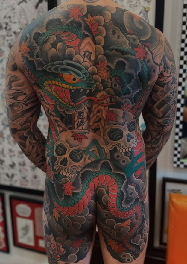 A full-body tattoo covering the back, arms, and legs featuring a colorful Japanese-style dragon, skulls, clouds, and maple leaves.