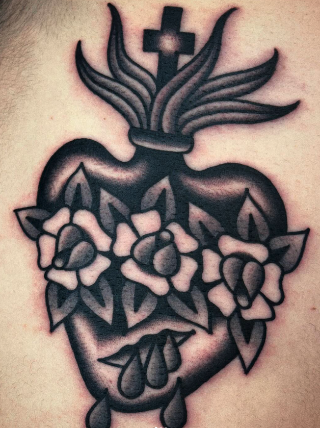 Tattoo of a traditional heart with a cross, flames, roses, and a dagger pierced through it.
