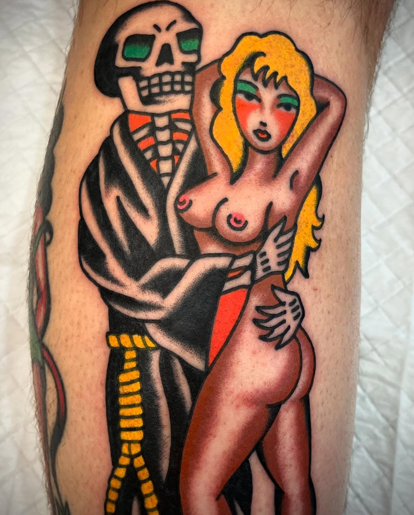 Tattoo of a skeleton man with green sunglasses holding a topless woman with long blonde hair and green eye makeup.