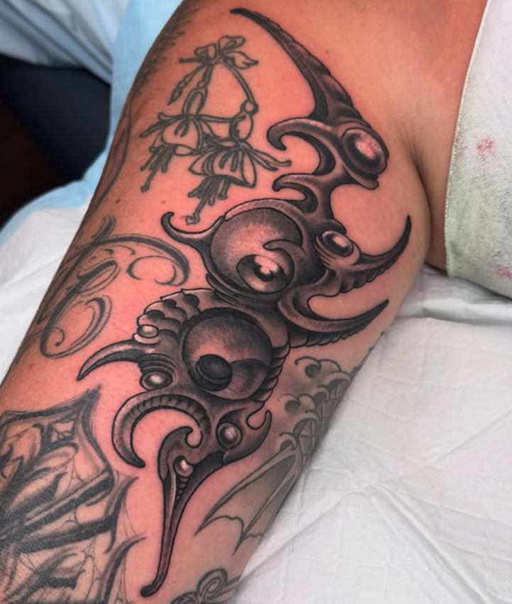 A black and gray tattoo of a tribal-style design featuring abstract shapes and swirling patterns on a person's upper arm or shoulder.