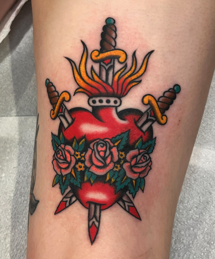 Colorful tattoo of a stylized human heart pierced by three swords, with a blooming rose bouquet around it, and flames above.