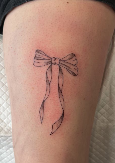 Tattoo of a simple bow with flowing ribbon on skin.