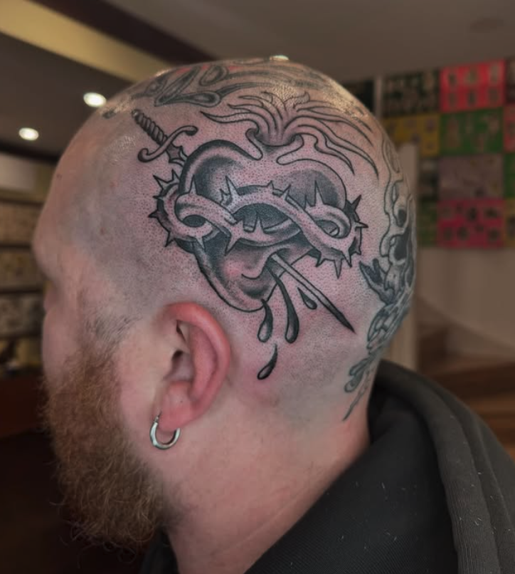 Tattoo of a snake wrapped around a sword on a person's scalp with a beard and hoop earring.