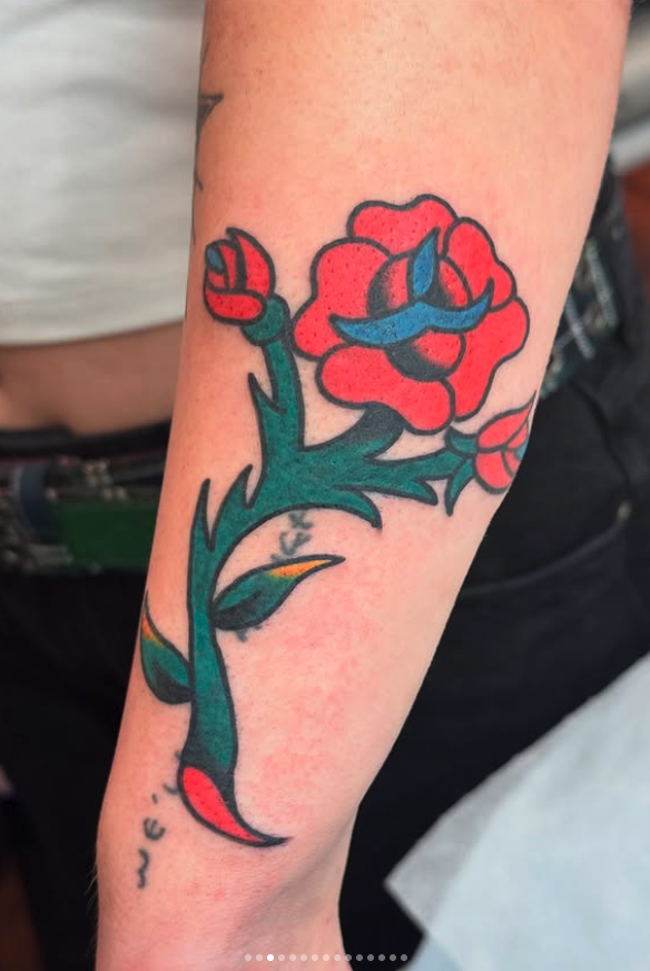 Tattoo of a red rose with a mustache and sunglasses, with the word 'QUE' written underneath.