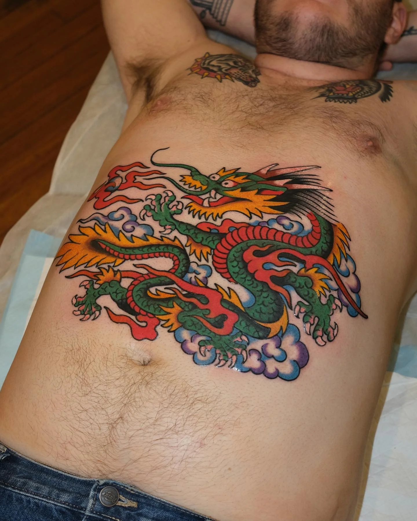 Colorful tattoo of a Chinese dragon on a man's chest, surrounded by clouds.