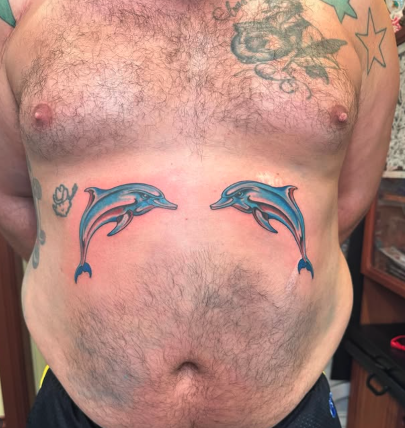 Tattoo of two blue dolphins swimming towards each other on a man's abdomen.