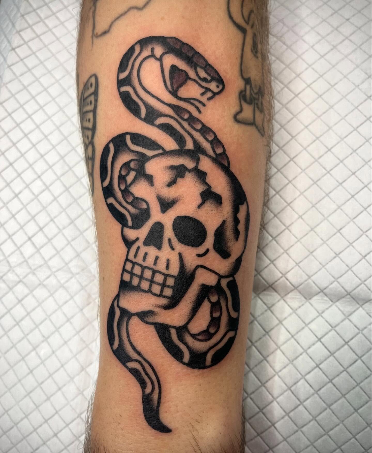 Tattoo of a snake intertwined with a human skull and a snake's head above, all in black ink.