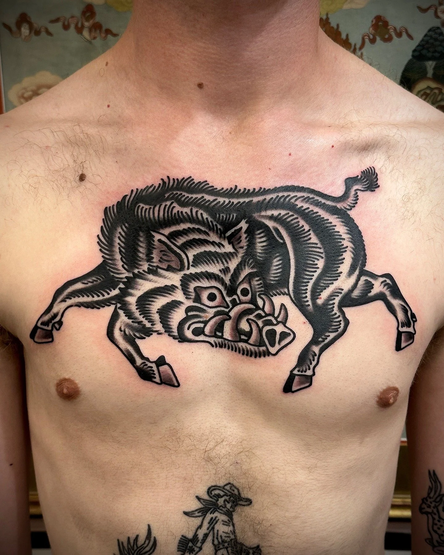 Tattoo of a fierce, stylized boar on the person's chest, with bold black lines and shading.