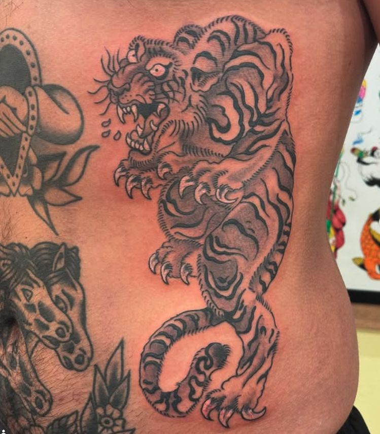 Tattoo of a fierce tiger with its mouth open, showing sharp teeth, and a detailed striped coat on a person's side.