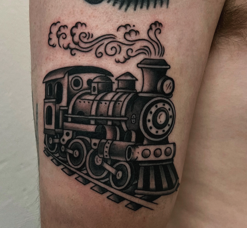 Black and gray tattoo of a steam locomotive train on skin, with smoke billowing from the chimney.