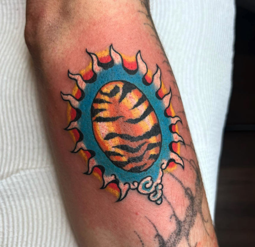 Colorful tattoo of a tiger-striped egg surrounded by a blue and fiery orange frame on a person's arm.