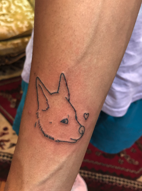 Tattoo of a dog's head with a small heart next to it on a person's arm.