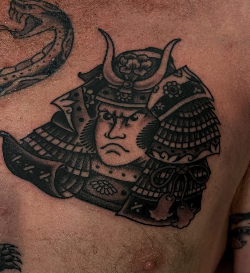 Tattoo of a samurai warrior with a stern face, wearing traditional armor and a helmet with horns, on a person's chest.