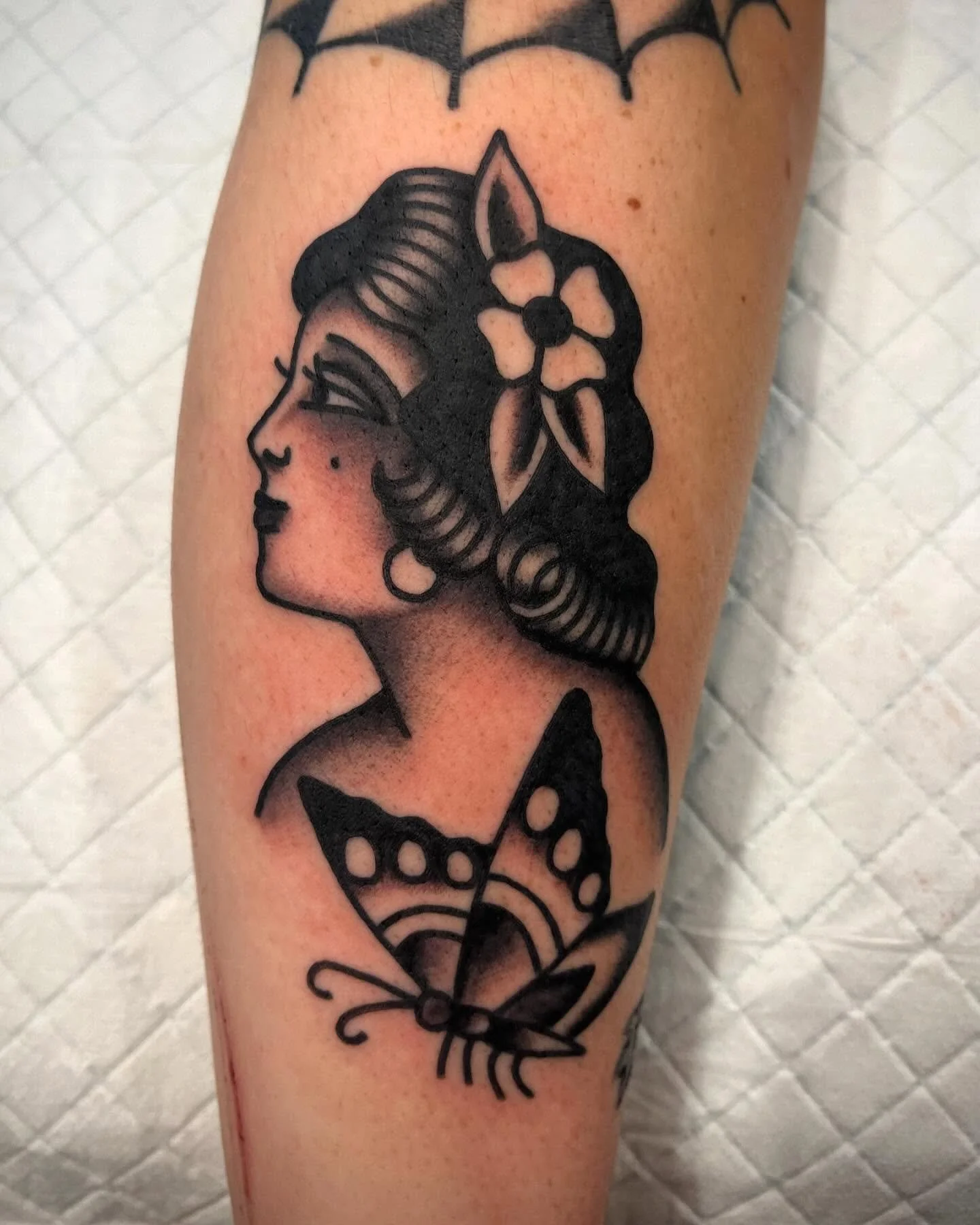 Black tattoo of a woman with flowers in her hair and a butterfly below her on skin.